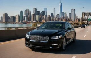 Black luxury sedan driving toward the New York City skyline on a sunny highway.