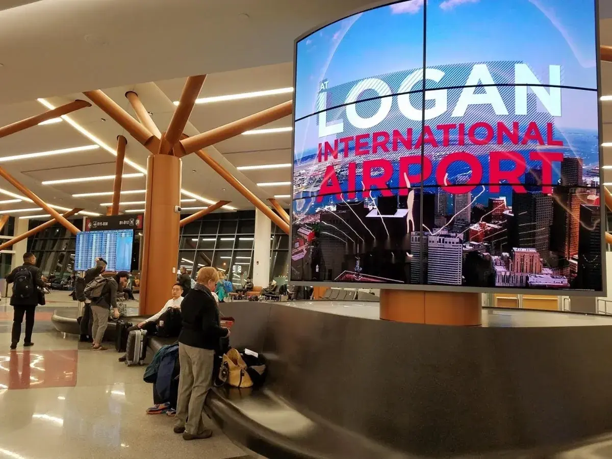 Boston Logan Airport Terminal B arrivals area featuring digital signage and passenger seating