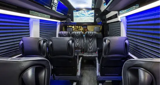 Luxury interior of an executive van featuring rows of black leather seats and blue ambient lighting
