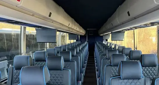 Spacious Motor Coach interior featuring ergonomic leather seating with blue piping and integrated overhead luggage storage