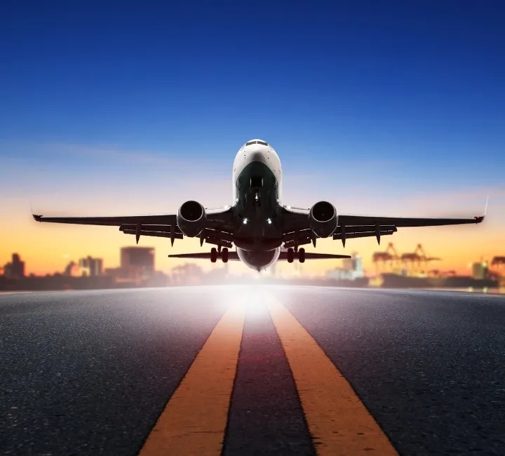 airplane taking off from airport runway at sunset with city